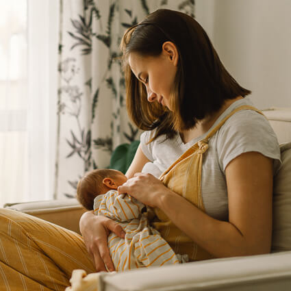 Parent nursing a baby in a chair near a window
