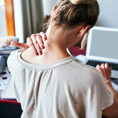 Woman at her desk rubbing the back of her tense neck while working