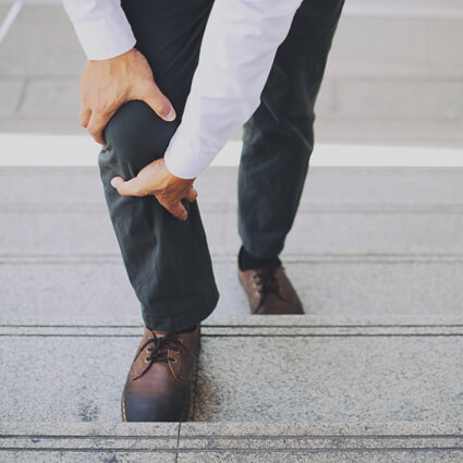 Man holding his leg in pain while climbing a flight of stairs, out of breath