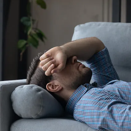Man resting on a couch with his arm over his face, worn down by chronic pain