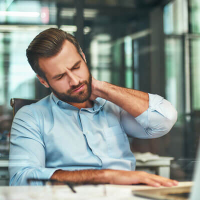 Man at his office desk rubbing his neck, tense from a stressful day