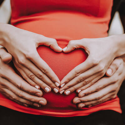 Couple making a heart shape with their hands on a pregnant belly