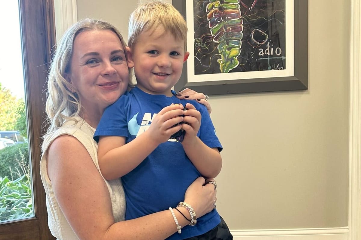 Mother holding her young son in front of framed spine artwork on the wall