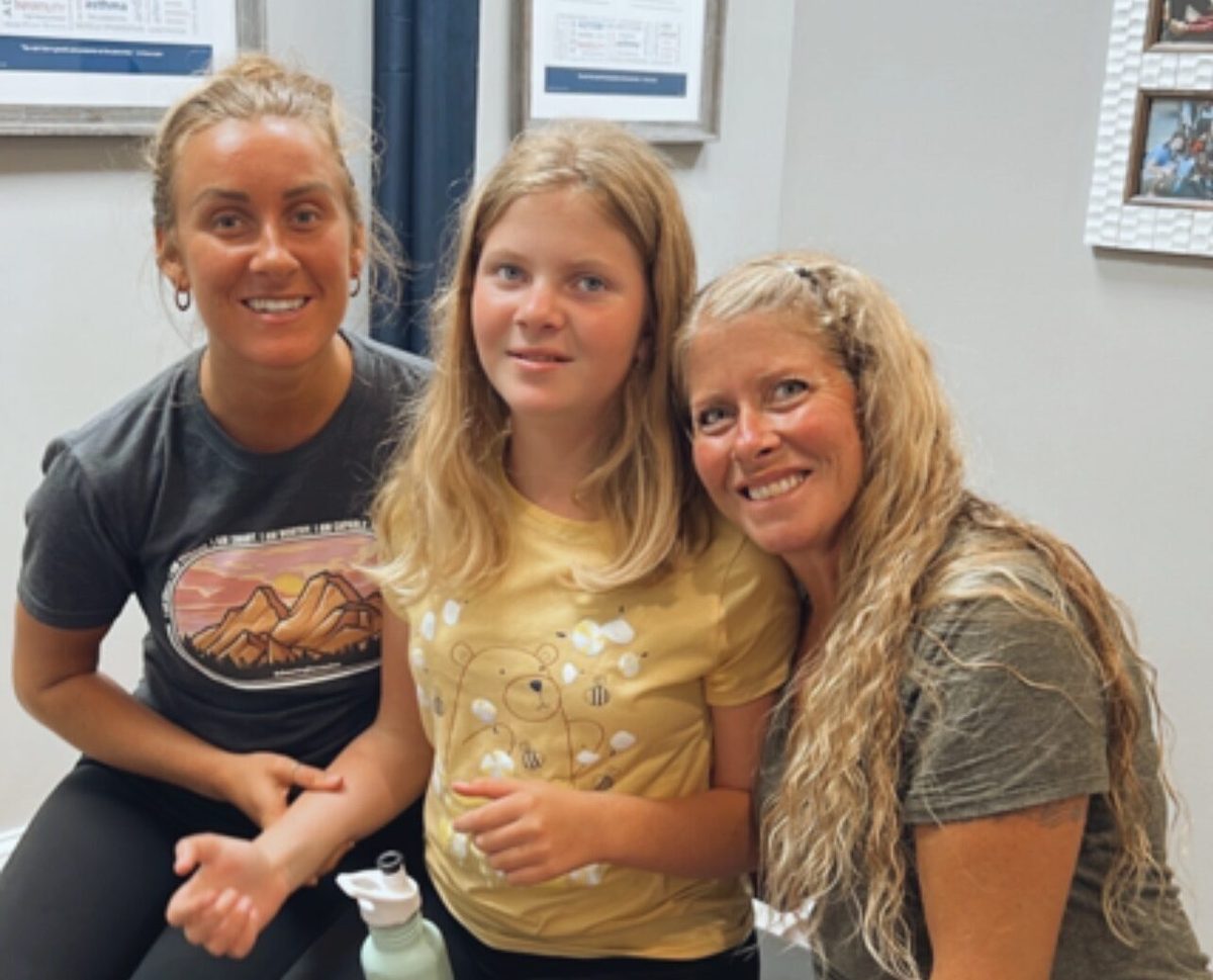 Two women and a young girl sitting together and smiling in a clinic waiting room