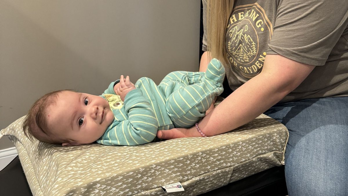 A woman holding a smiling baby in striped pajamas on a changing pad, one hand supporting the baby's legs