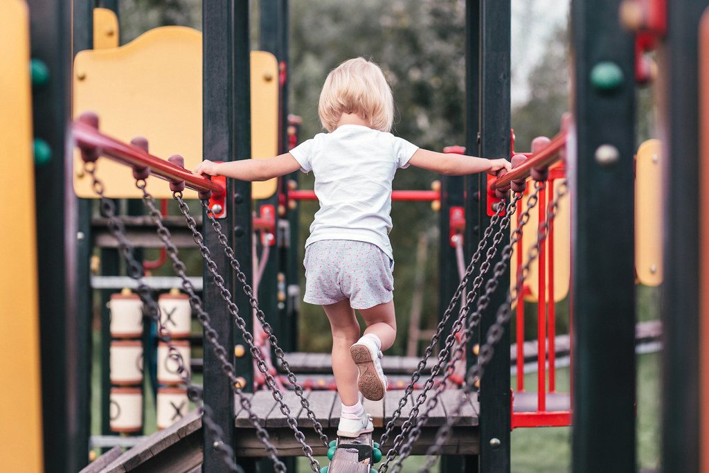 A young child climbs across a rope bridge on a playground structure.
