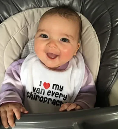 Clara as a smiling baby in an I love my Van Every chiropractor bib