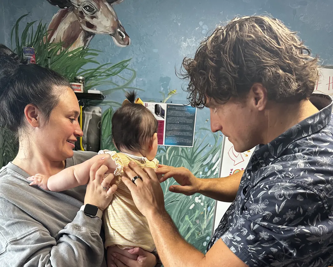 Dr. Zach Conner gently adjusting a baby as mom holds on