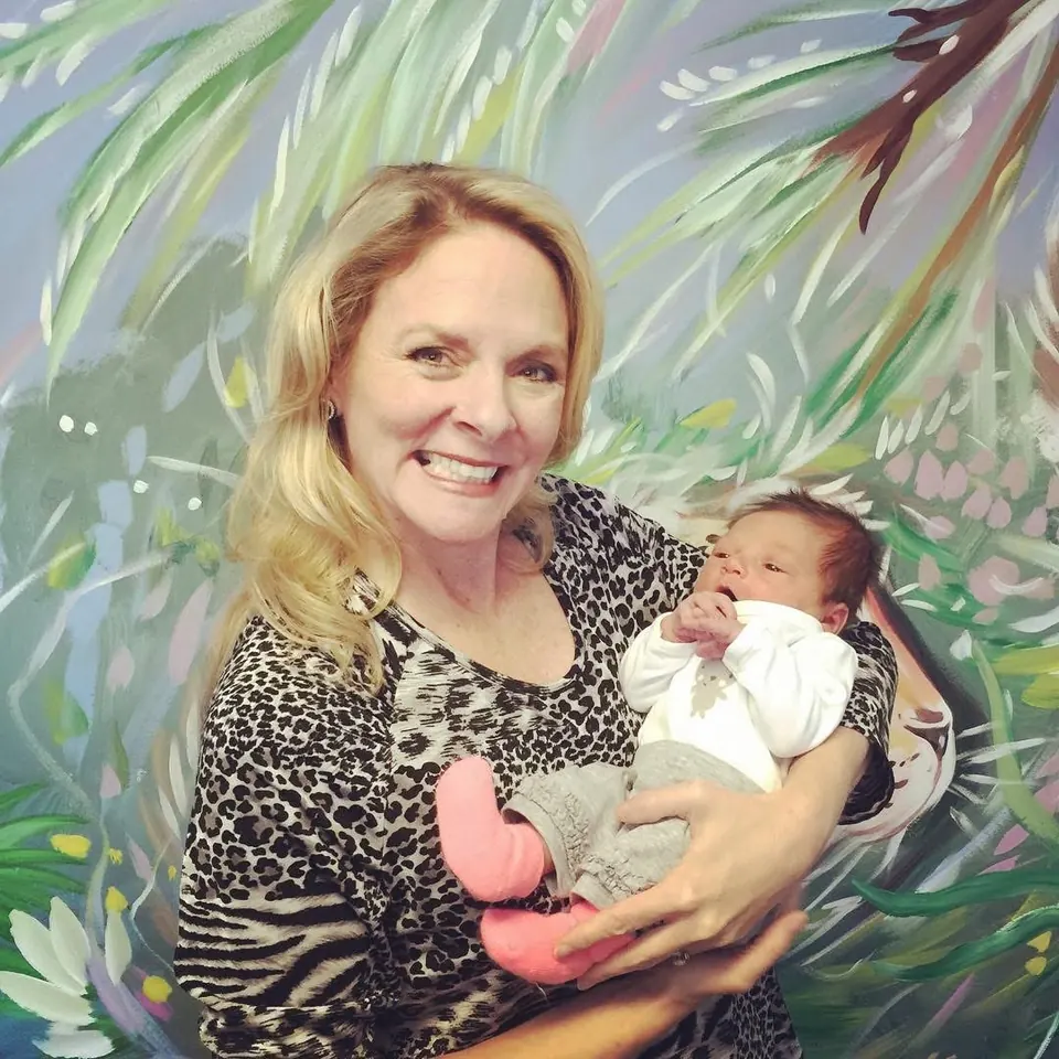 Dr. Anna Saylor smiling with a newborn in front of our jungle mural