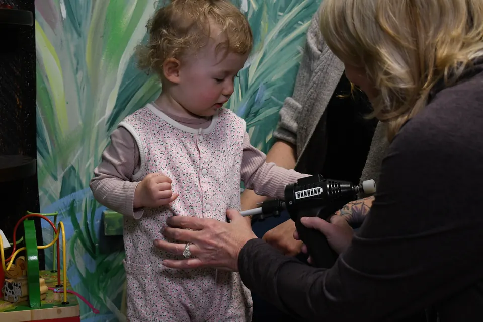 Dr. Anna Saylor checking a curious toddler in front of our painted jungle wall