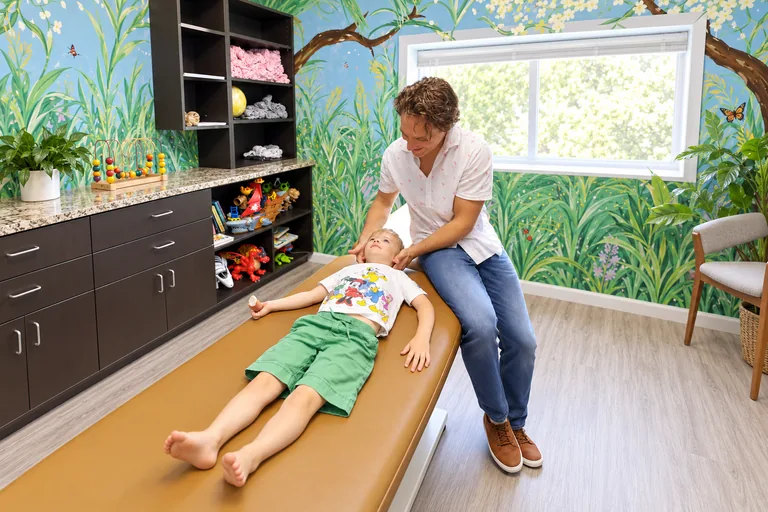 Dr. Zach Conner caring for a child in our jungle-mural treatment room